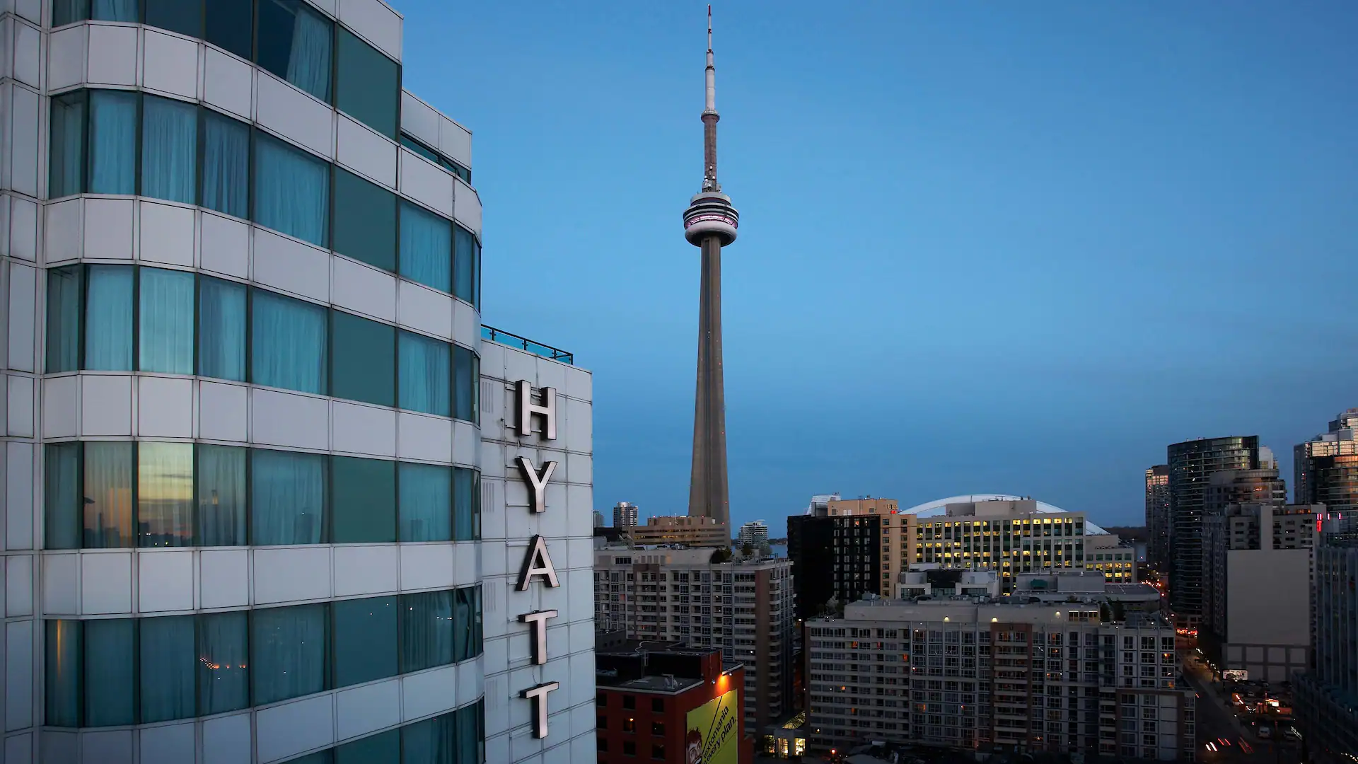 Exterior of Hyatt Regency Toronto with the CN Tower and downtown Toronto skyline at dusk
