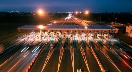 aerial view of a large toll gantry at night with streaming lights.
