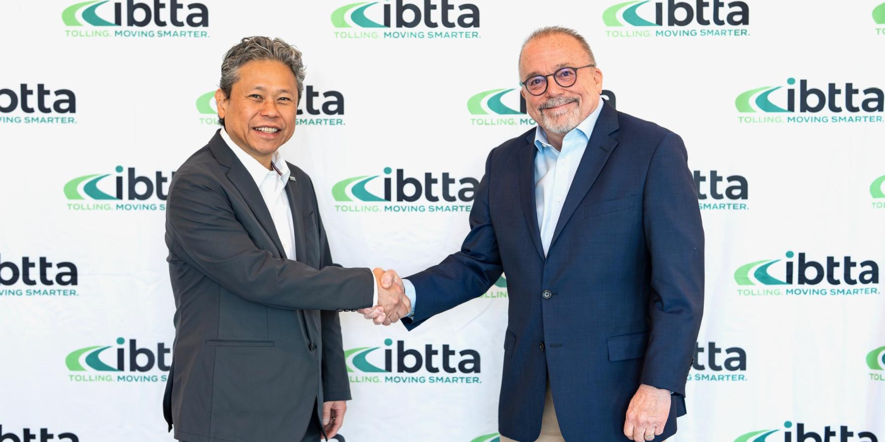 two men handshaking in front of an IBTTA Step & Repeat showing IBTTA's logo