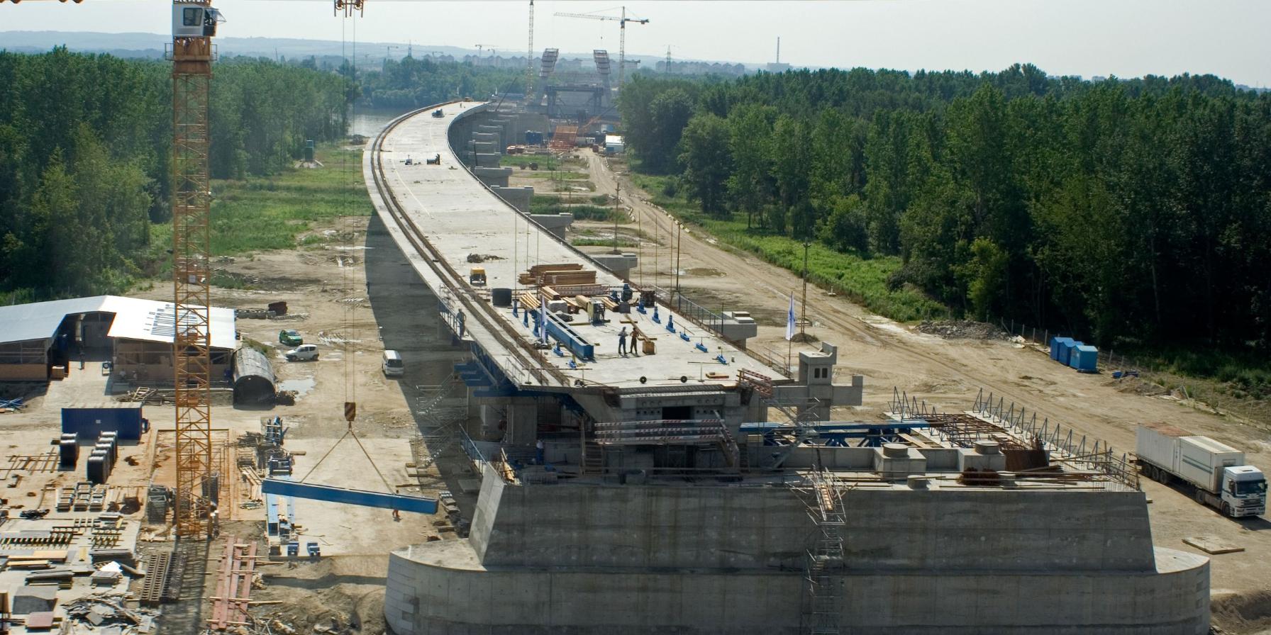 Concrete bridge under construction with cranes and workers assembling the roadway deck.