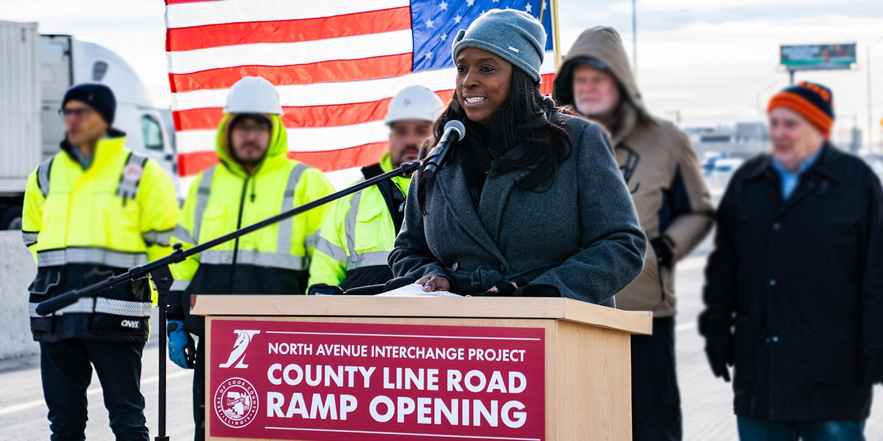 Cassaundra Rouse speaking at podium with American Flag in background