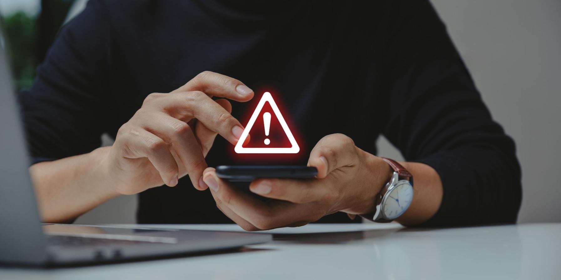 Person holding a smartphone with a warning alert icon displayed above the screen
